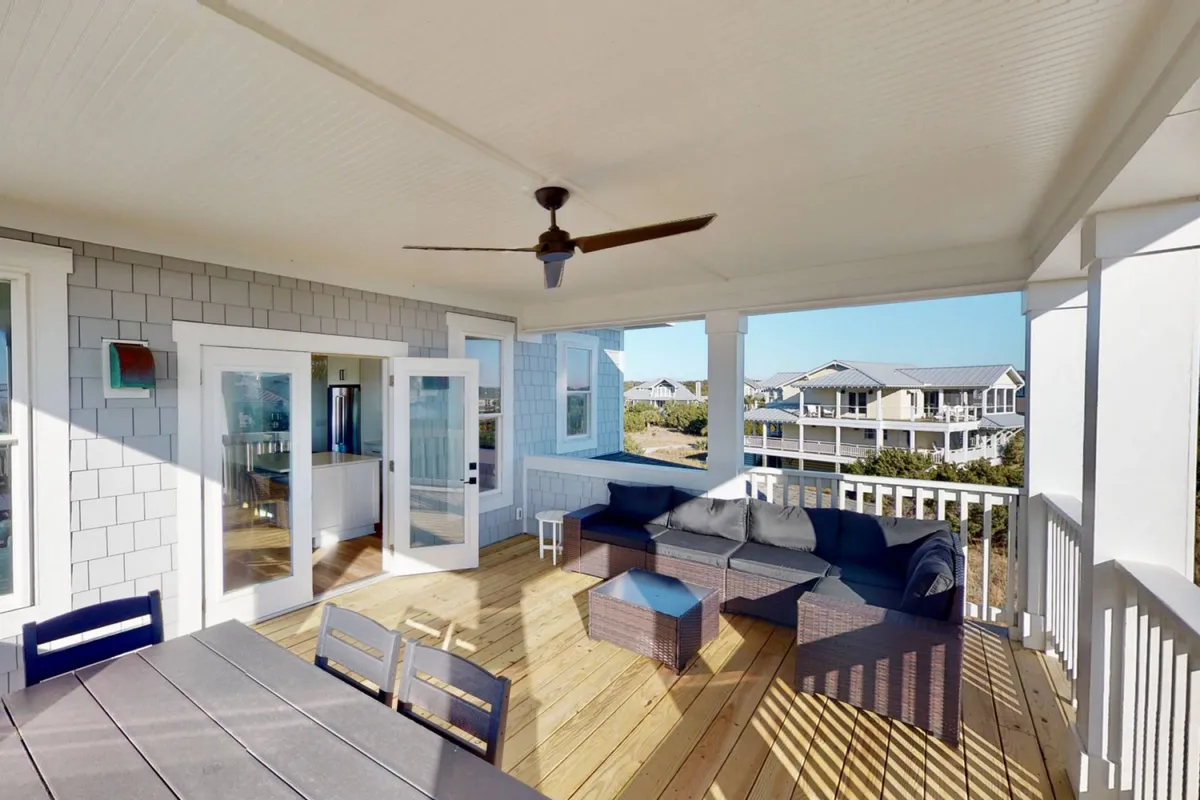 A casual, welcoming outdoor seating area and dining table on the deck, overlooking neighboring houses. The atmosphere is friendly and designed for socializing, eating outdoors, or unwinding with friends after a day of golf or beach activities.