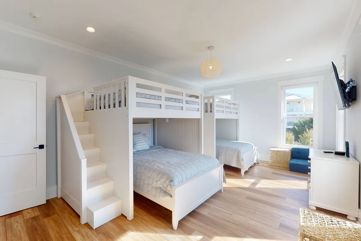 A playful and cozy children’s bunk room with sturdy bunk beds, a bright window, and a soft seating area. The mood is fun and inviting, perfect for kids to play, read, or unwind after a day at the beach.
