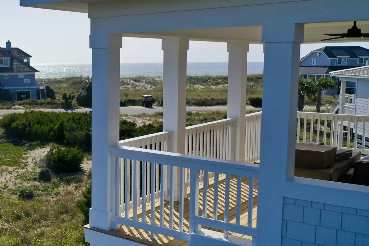 A tranquil deck scene featuring a sturdy railing, comfortable seating, and sweeping ocean views across the horizon. The landscape and light evoke both the serenity of morning coffee and the magic of sunset drinks.