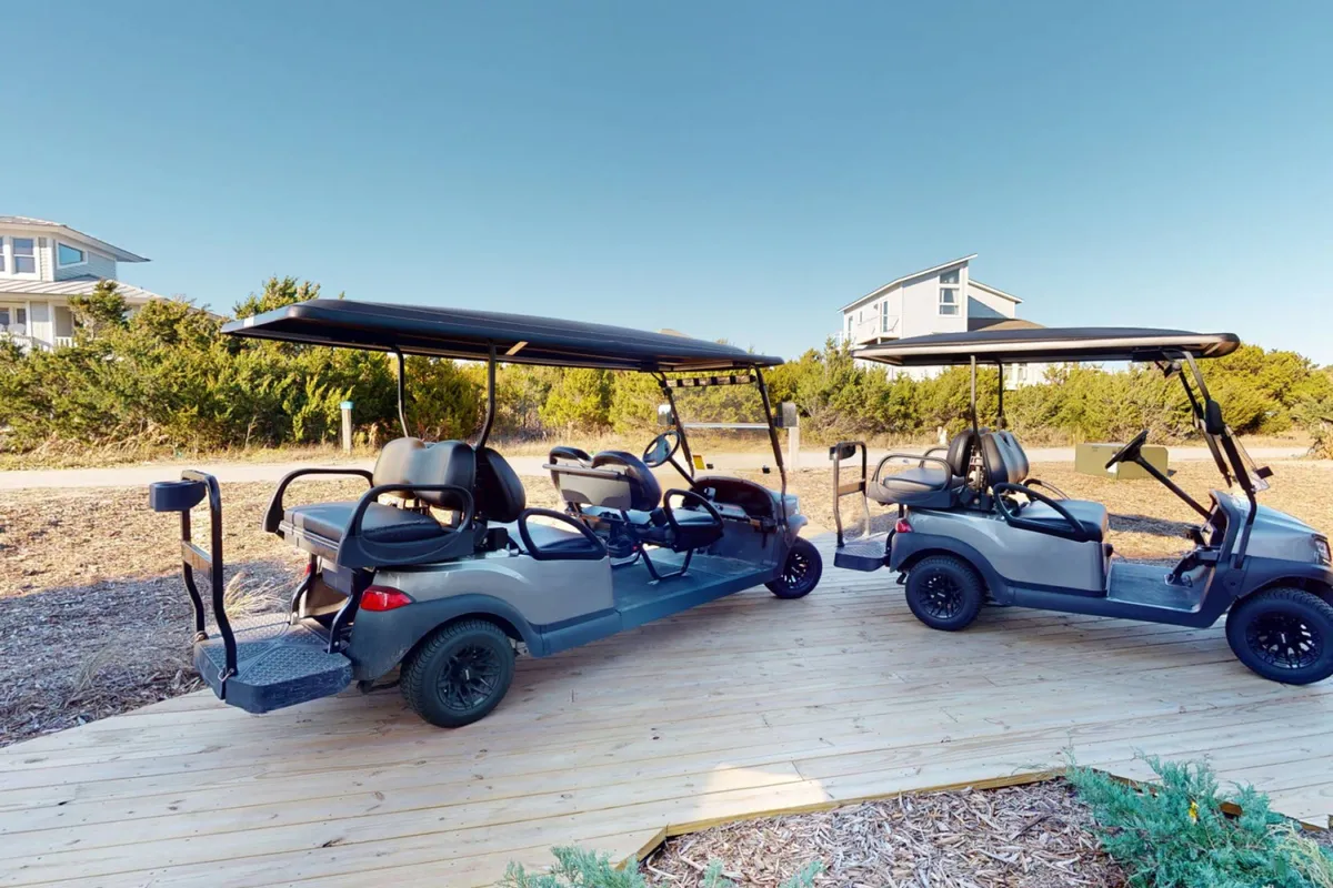 This image showcases two large golf carts parked on a wooden platform surrounded by lush greenery. The setting suggests easy access to transportation for island exploration and embodies the laid-back, adventurous spirit of Bald Head Island.