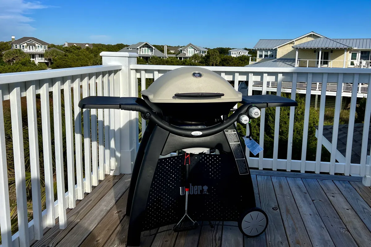A deck area with a gas grill set up beside the railing, overlooking a scenic view. The setup suggests a convivial environment for barbecuing and hosting outdoor feasts while enjoying the fresh ocean air.