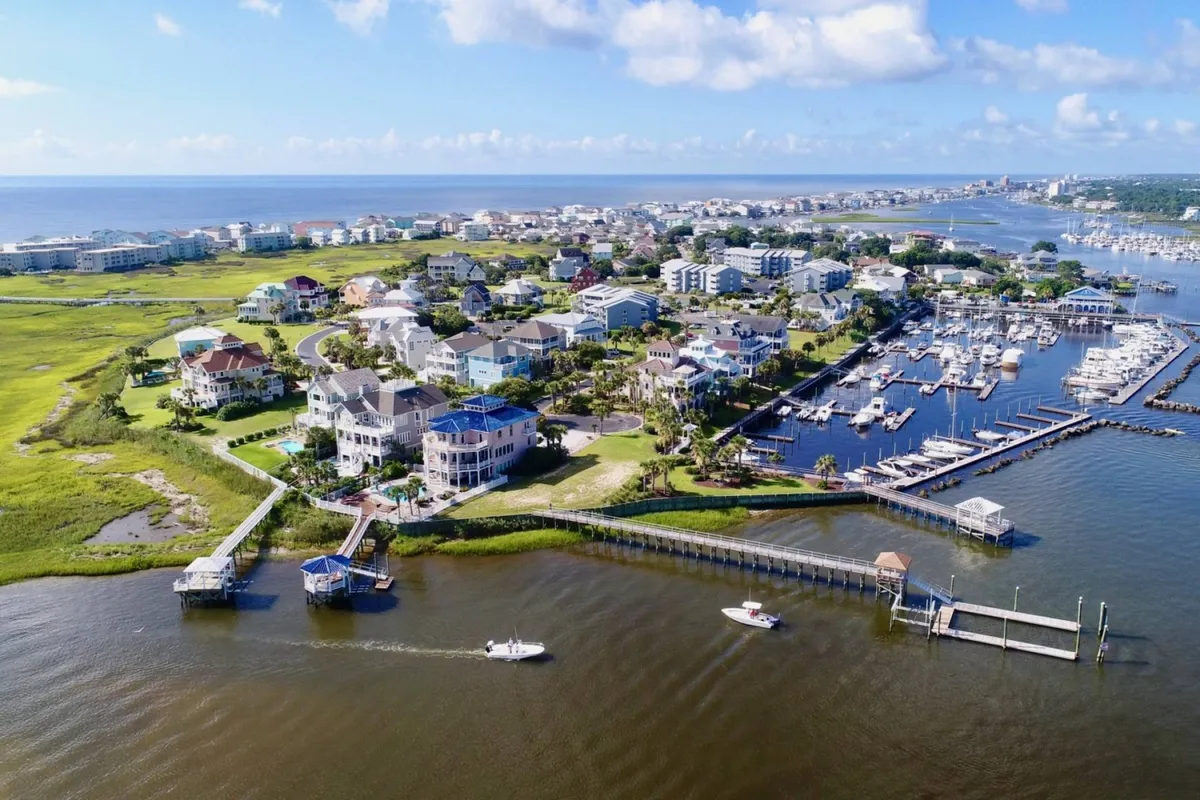 A scenic shot of the marina with boats docked, framed by residential homes and lush green spaces. The tranquil water and inviting neighborhood atmosphere highlight the island’s resort lifestyle and easy access to activities and social venues.